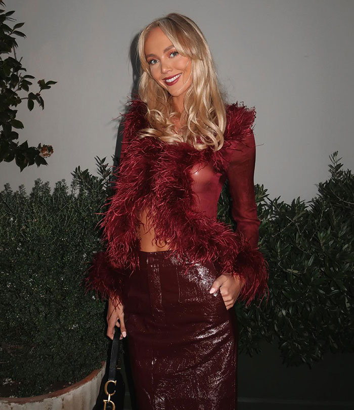 Annie Knight in a red feathered outfit, posing outdoors with greenery, linked to hospitalized after health issues. Annie Knight in a red feathered outfit, posing outdoors with greenery, linked to hospitalized after health issues.