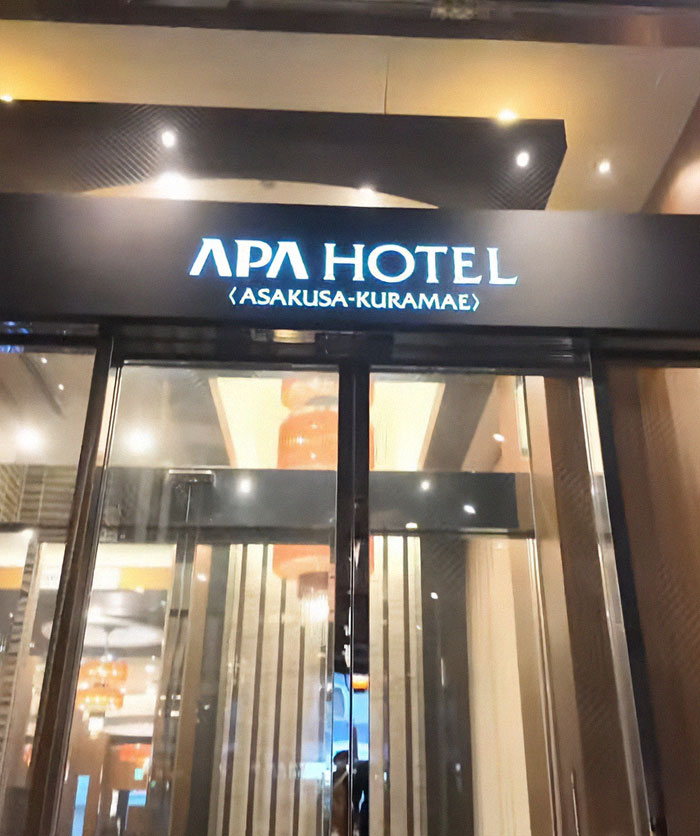 Entrance of APA Hotel Asakusa-Kuramae at night with illuminated sign, related to solo traveler spotting person hiding under hotel bed.
