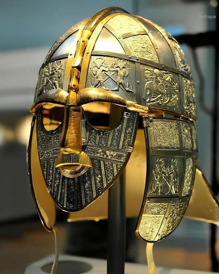 Highly detailed archeological helmet with intricate gold and silver artwork displayed in a museum exhibit on archeology and art.