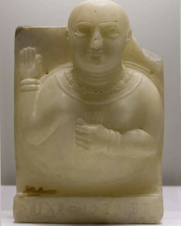 Ancient carved stone figure with raised hand and detailed necklace, an archeological art wonder from early civilizations.