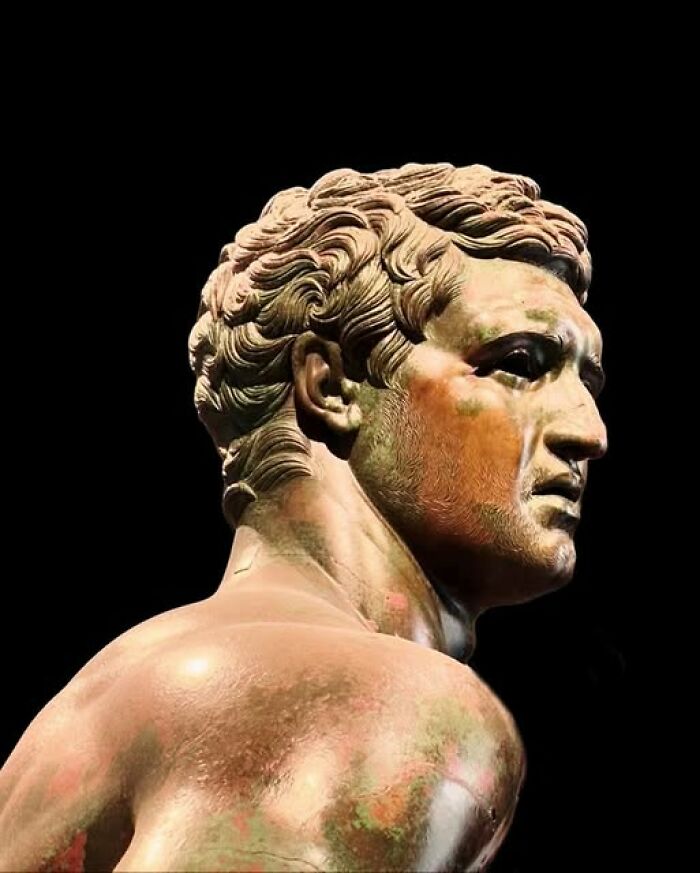 Ancient bronze statue of a male figure showcasing detailed archeology and art craftsmanship against black background