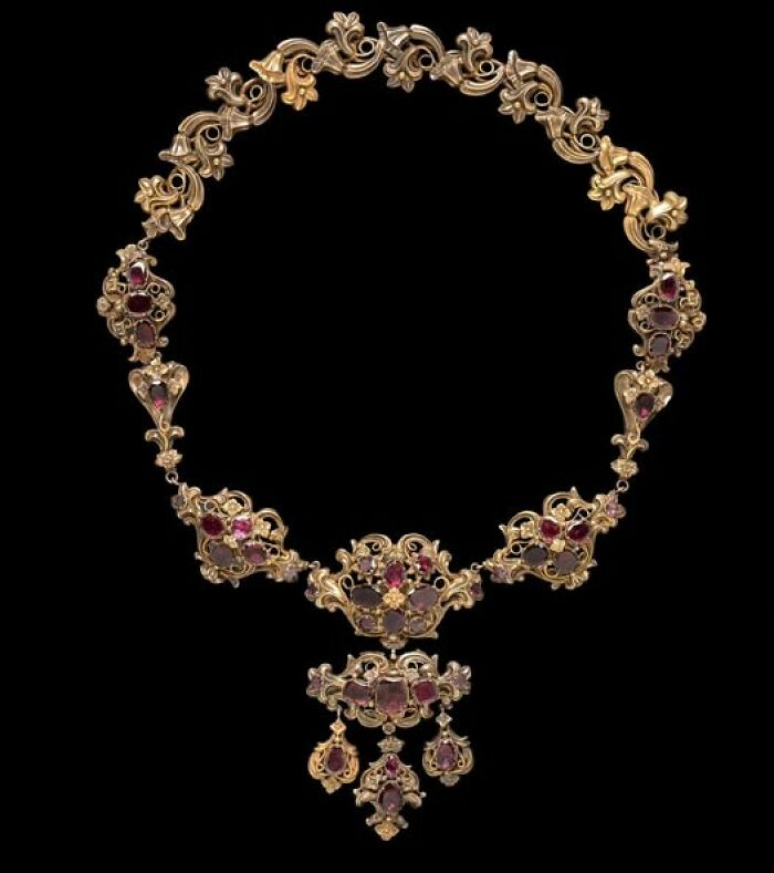 Intricately designed archeological gold necklace adorned with red gemstones, showcasing art and craftsmanship from ancient times.