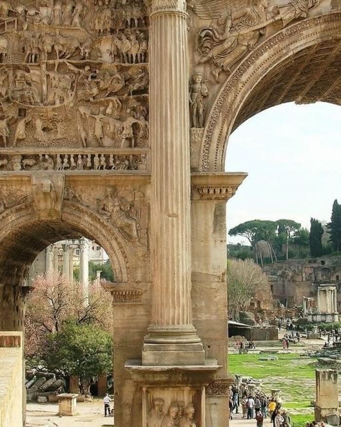 Ancient archeological ruins featuring detailed stone carvings and columns with tourists exploring historic site outdoors.