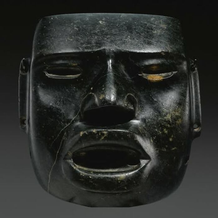Black ancient stone mask with worn features, an archeological wonder showcasing art and craftsmanship from a past civilization.