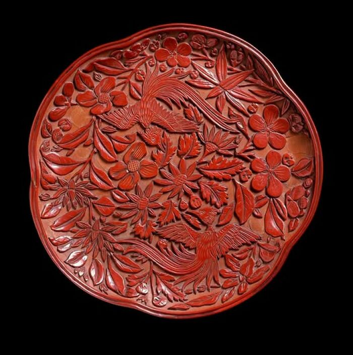 Intricately carved red lacquer plate featuring birds and flowers, an example of archeology and art craftsmanship.