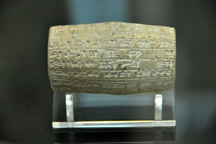 Ancient clay artifact with cuneiform writing displayed on a clear stand, showcasing archeology and art discovery.