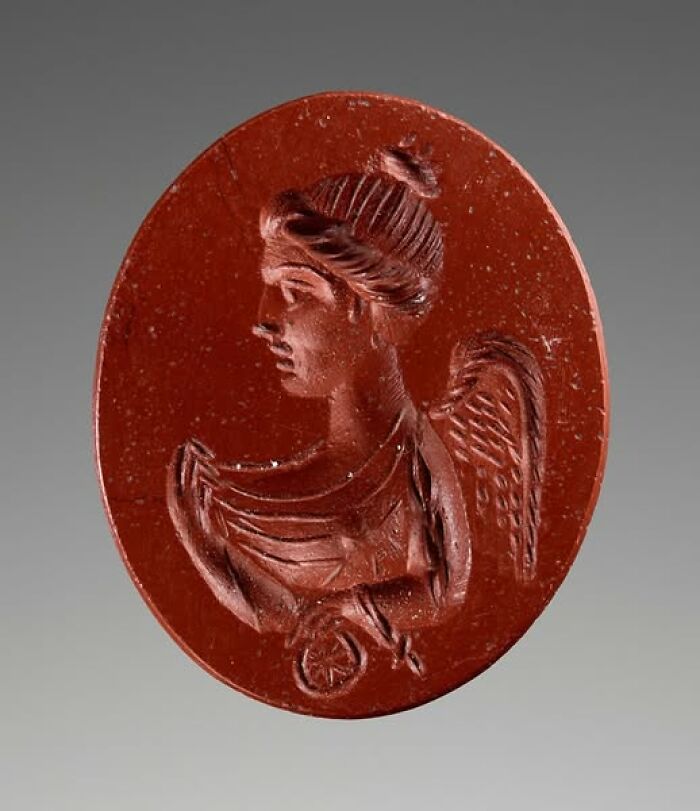 Red ancient carved gem depicting a winged figure, an archeological wonder showcasing art and craftsmanship.