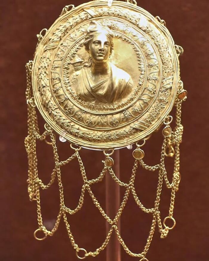Intricately designed ancient gold artifact featuring a relief of a female figure with decorative chains, showcasing archeological art.