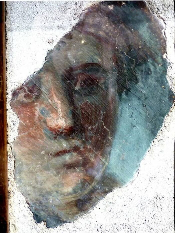 Ancient archeological art fragment depicting a human face on a weathered stone surface with faded colors.