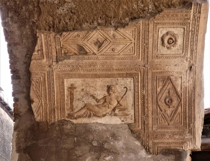 Ancient archeological art carving on a weathered wall depicting a reclining figure with a staff in detailed stone relief.