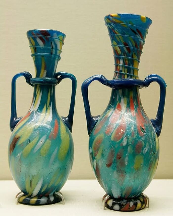 Two colorful ancient glass vases with handles, showcasing archeological art and craftsmanship from historical wonders.