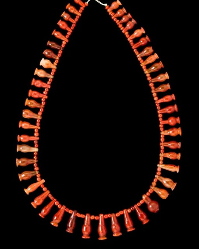 Ancient necklace made of small amphora-shaped beads in red hues, an archeology and art archeological wonder on black background.