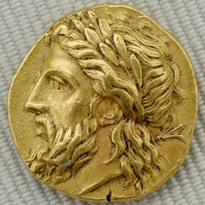 Ancient gold coin with detailed male profile wearing a laurel wreath, representing archeology and art history.