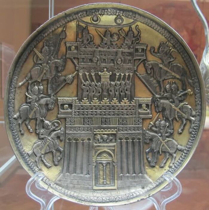 Ancient metal plate featuring detailed archeological art of a fortified castle with warriors on horseback.