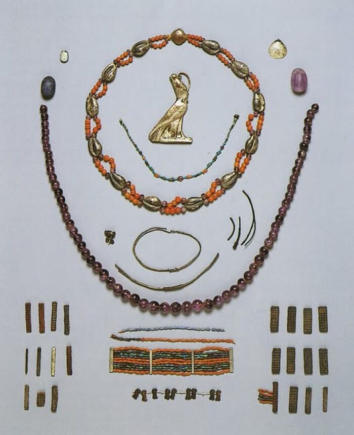 Ancient archeological jewelry and artifacts including beaded necklaces and gold pendants displayed against a white background.