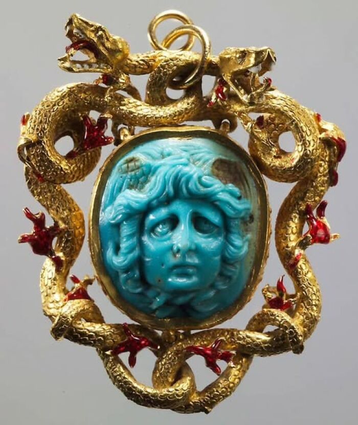 Intricate archeological pendant featuring a turquoise carved face surrounded by coiled gold serpents and red accents.