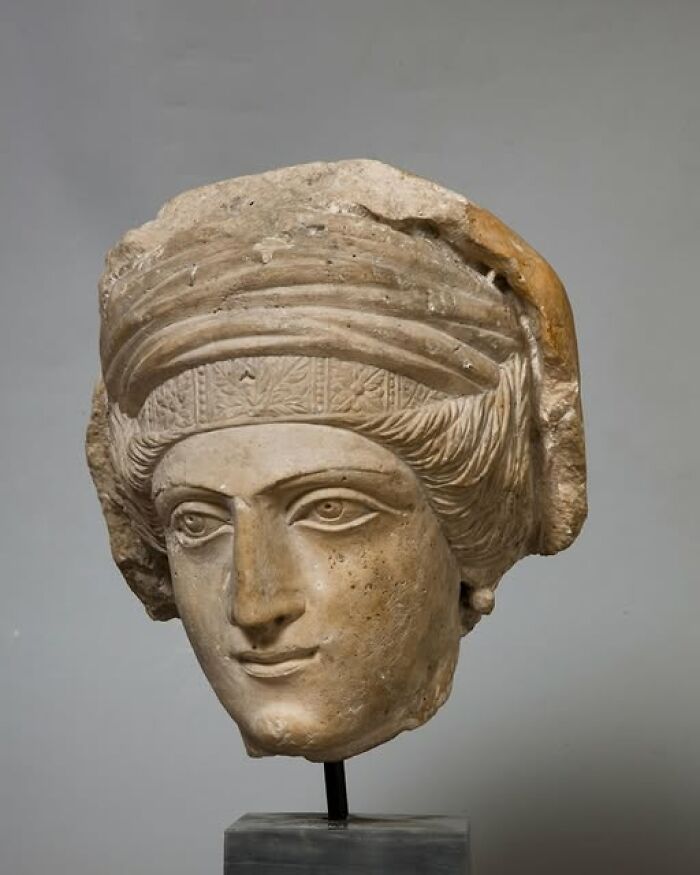Ancient stone sculpture of a head with intricate headdress, showcasing archeology and art from historical times.