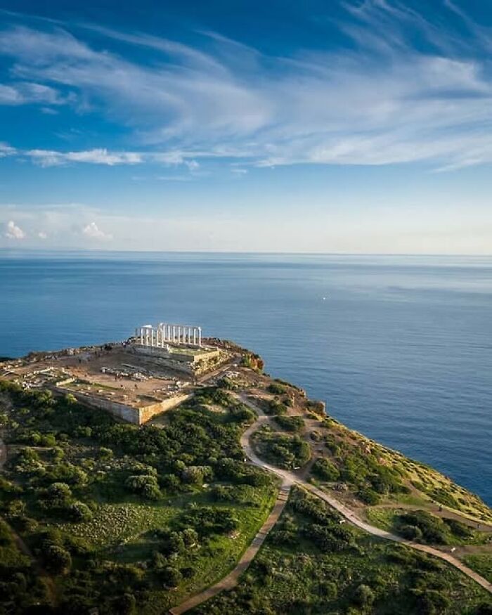 Ancient archeological wonder on coastal cliff with ruins and columns overlooking calm blue ocean under a bright sky.