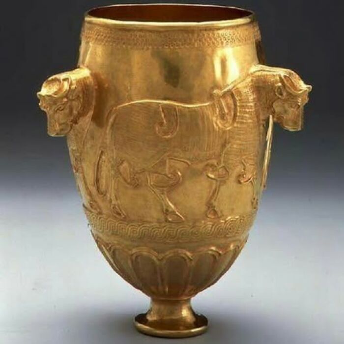 Golden ancient cup with intricate animal art and sculpted bull heads, an archeological wonder of historic craftsmanship.