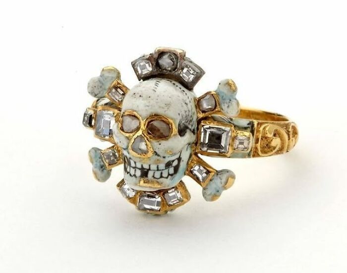 Gold and enamel archeological ring featuring a skull and crossbones design with embedded gemstones, showcasing ancient art.