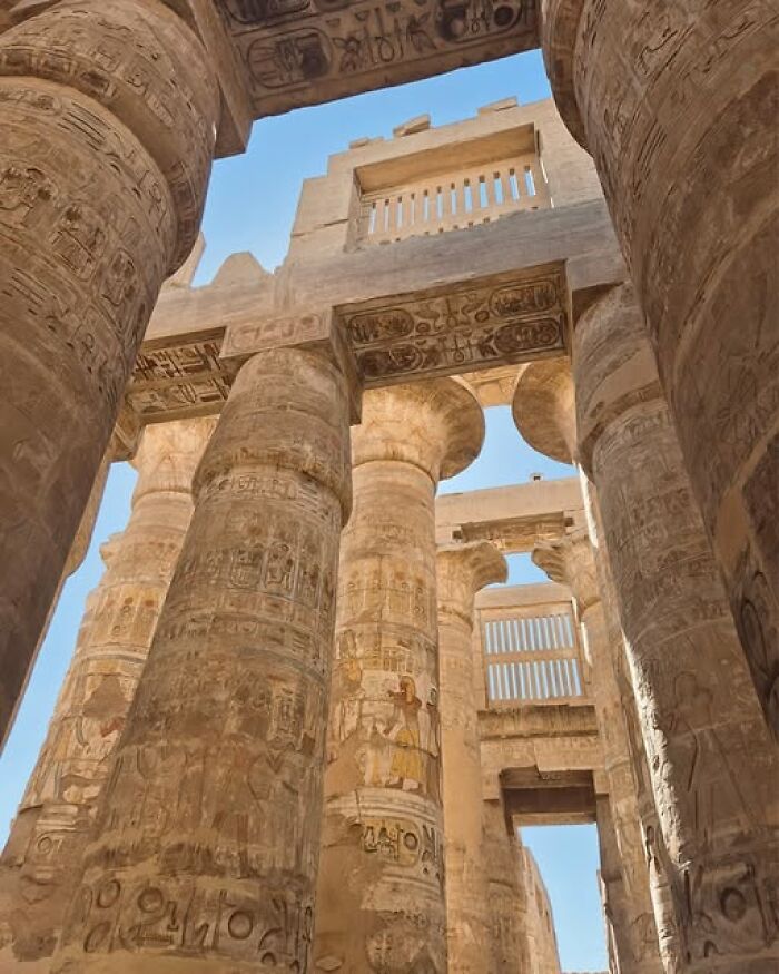 Ancient archeological pillars with detailed carvings and hieroglyphs under clear blue sky showcasing archeology and art.