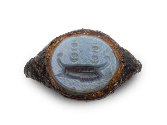 Ancient archaeological artifact with carved blue gemstone depicting a boat, showcasing archeology and art craftsmanship.