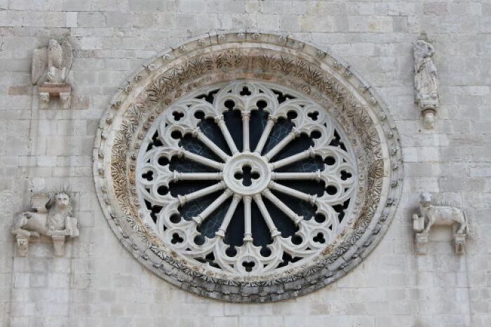 Intricate stone rose window on historic building showcasing archeology and art in ancient architectural design.