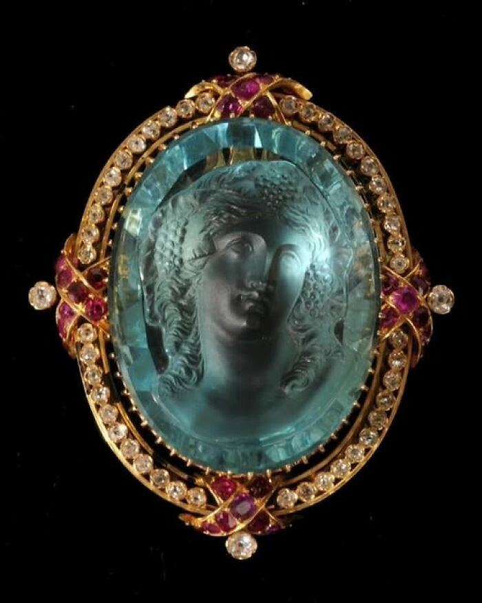 Ornate archeological art pendant featuring an ancient carved blue gem portrait with gold and ruby details.