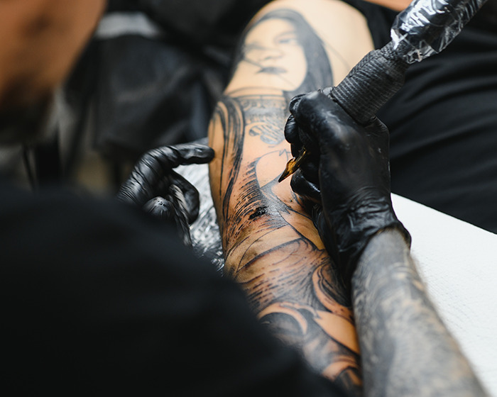 Tattoo artist wearing black gloves creating detailed tattoo sleeve on client's arm in a professional studio setting.