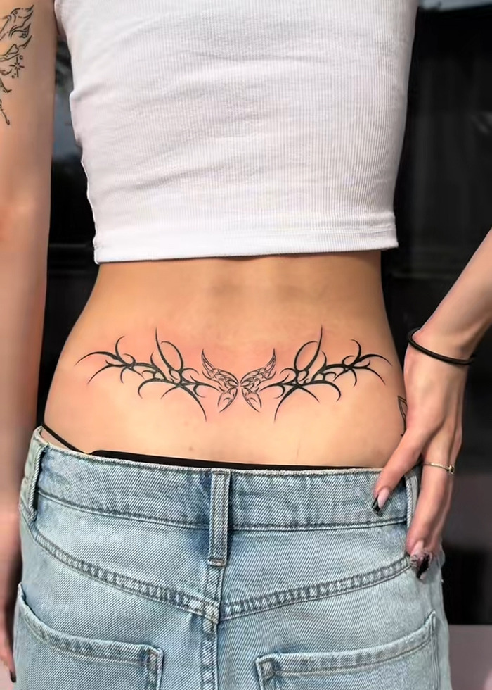 Lower back tattoo with butterfly and tribal design, illustrating the tattoo boom and expert insight on cooling off in 2025.