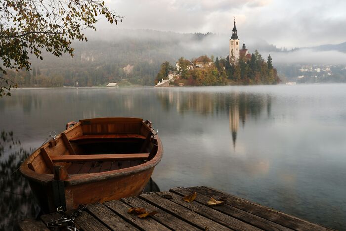 Wooden boat on calm lake near island with church, showcasing wonders that prove the world is still full of magic.
