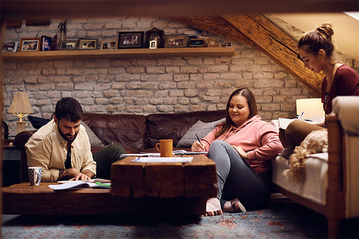 Three young adults studying together in a cozy living room, reflecting on asking roommates to leave situations.