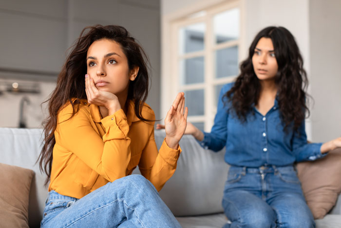 Two women having a tense conversation on a couch, illustrating how food talk triggers her due to son’s autism. Two women having a tense conversation on a couch, illustrating how food talk triggers her due to son’s autism.