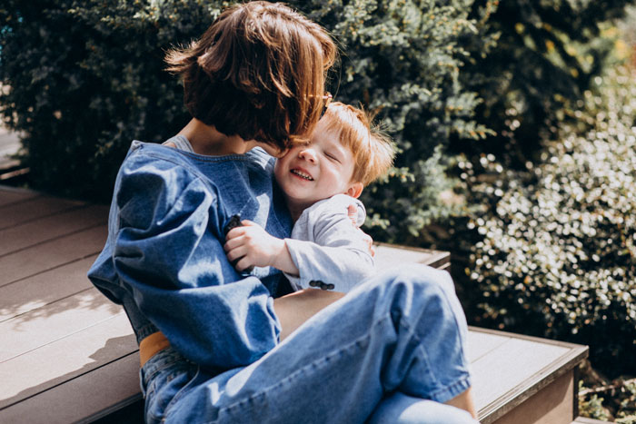 Woman sitting outside with her son who has autism, sharing a tender moment while embracing and smiling together. Woman sitting outside with her son who has autism, sharing a tender moment while embracing and smiling together.