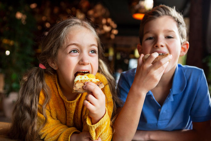 Young children eating pizza, illustrating challenges related to food talk and autism triggers in family dynamics. Young children eating pizza, illustrating challenges related to food talk and autism triggers in family dynamics.
