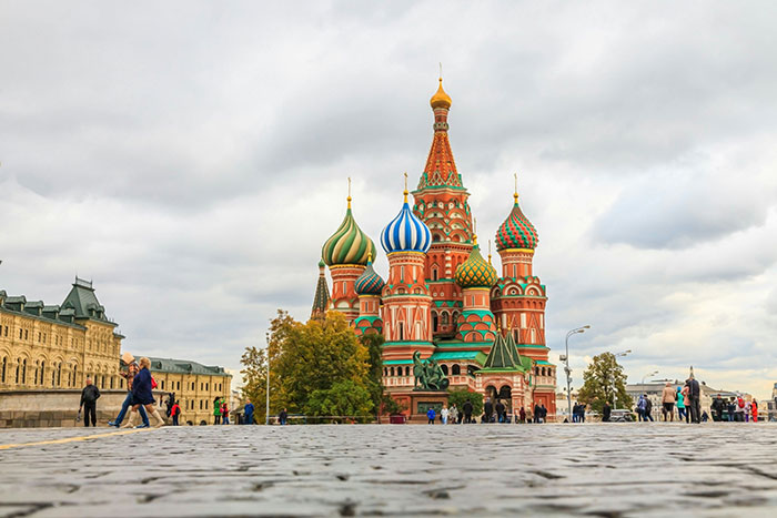 Colorful domes of Saint Basil’s Cathedral in Moscow with people walking on the cobblestone street under cloudy sky.