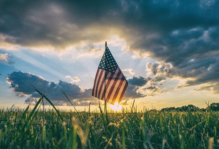 American flag in grass field at sunset with dramatic clouds, symbolizing the biggest elephant in the room concept.