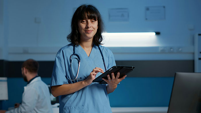 Female medical professional in blue scrubs using a tablet in a modern clinic, highlighting the biggest elephant in the room.