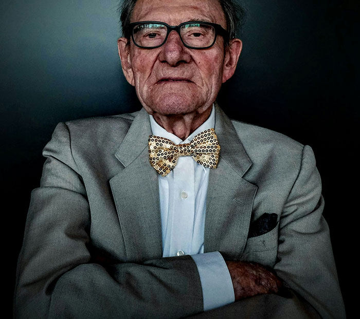 Elderly man in glasses and patterned bow tie looking serious, representing massive awkward truths ignored by everyone.