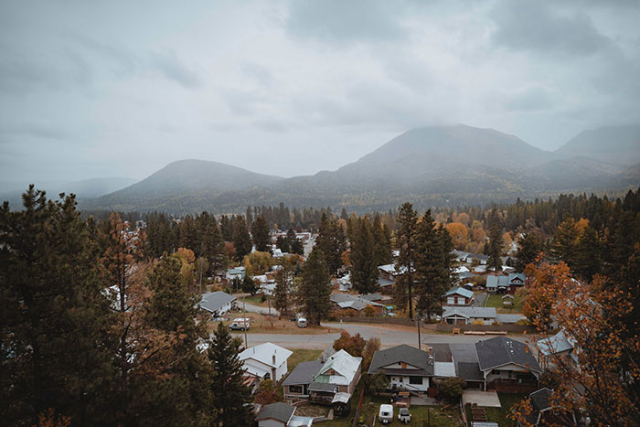 Small town homes surrounded by trees and mountains on a cloudy day, capturing moments of massive awkward truths ignored.
