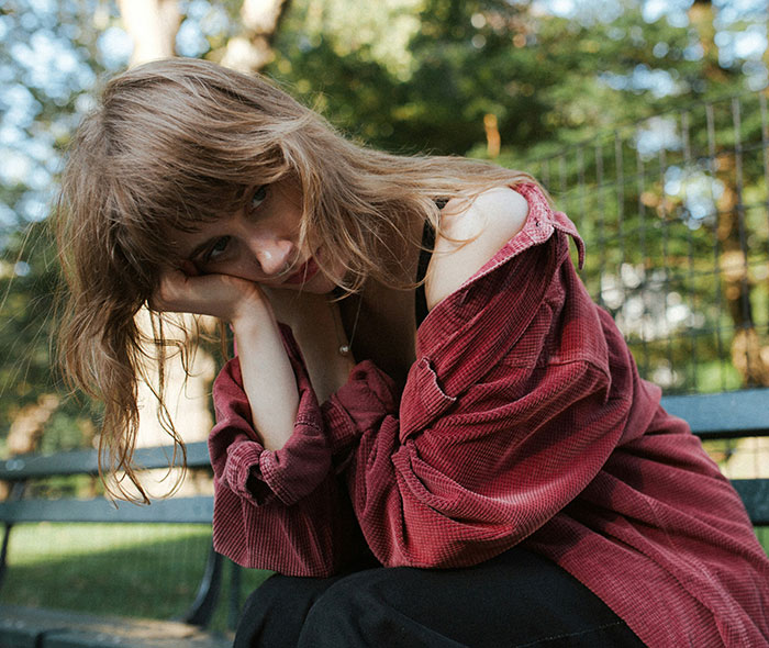 Young woman in a red jacket sitting on a bench looking pensive, capturing a moment of massive awkward truths ignored.