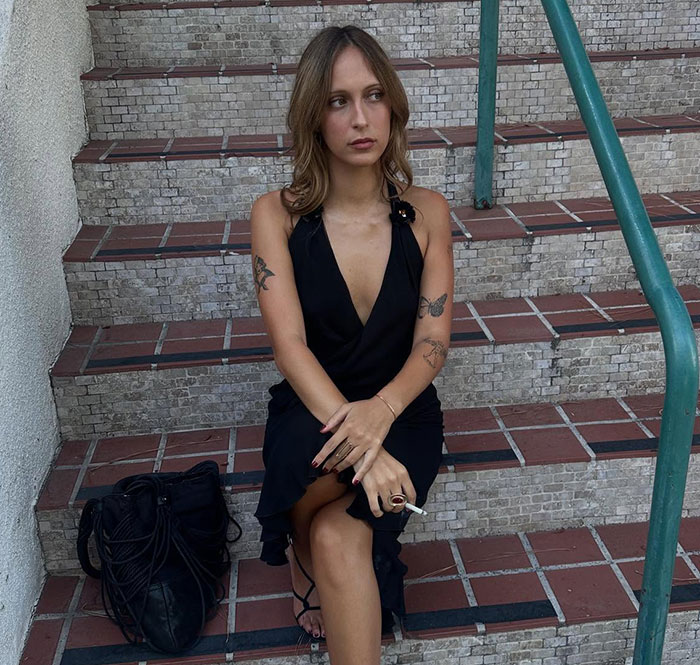 Young woman with tattoos in a black dress sitting on tiled stairs, relating to Gigi and Bella Hadid secret sister news. Young woman with tattoos in a black dress sitting on tiled stairs, relating to Gigi and Bella Hadid secret sister news.