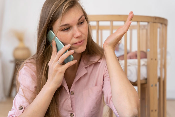 Young woman in pink shirt on phone, looking frustrated while caring for two kids at home alone for days