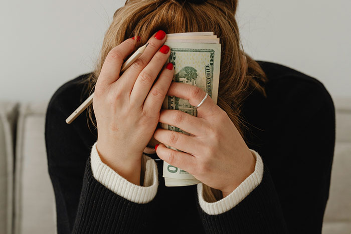 Woman covering face with hands and cash, illustrating internet debates on whether paying for hen parties is excessive.