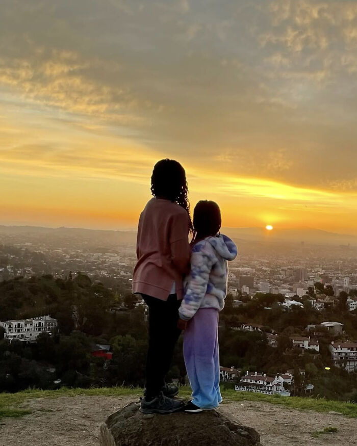 Two children standing on a rock overlooking a city at sunset, reflecting on Charlize Theron's children respecting her.