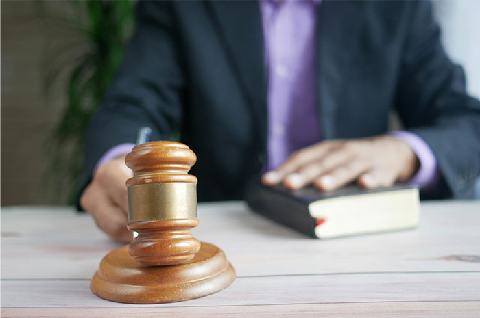 Person in a suit with hand on a book and gavel on the table representing HR employees handling background checks.
