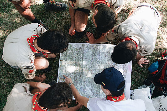 Group of scouts examining a map outdoors, illustrating teamwork and problem-solving relevant to HR background checks.