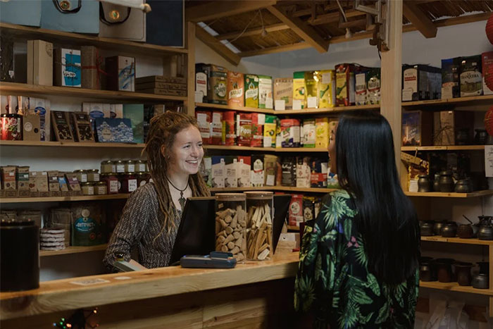 Two women talking at a small retail store counter, illustrating HR employees sharing the worst background checks encountered.