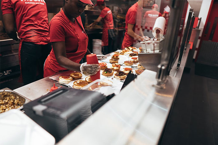 Fast food workers preparing burgers and fries, illustrating challenges HR employees face during background checks.