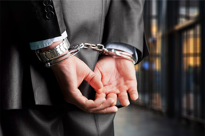 Close-up of a man in a suit wearing handcuffs, illustrating issues HR employees faced during background checks.